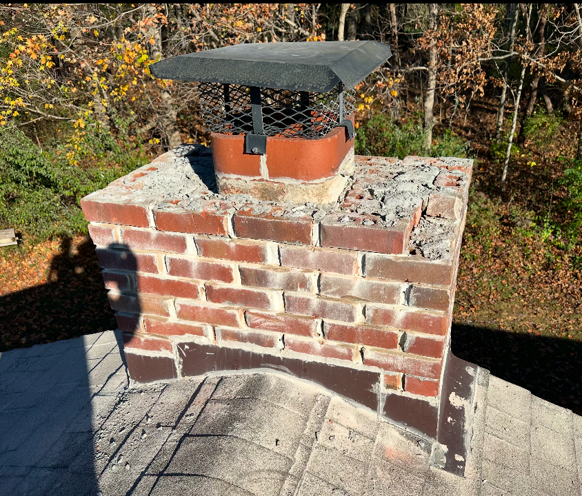 Brick chimney on a rooftop with a black metal cap in need of a chimney cap & masonry repair