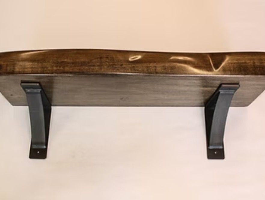 Wooden fireplace mantle with two black metal brackets against a light wall