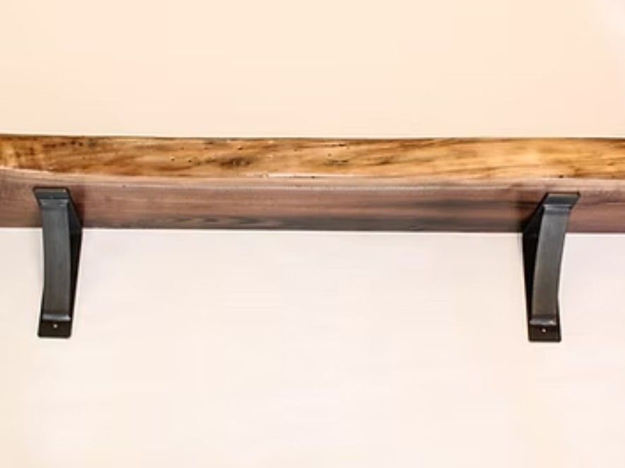 Wooden fireplace mantle with black metal brackets mounted on a light wall