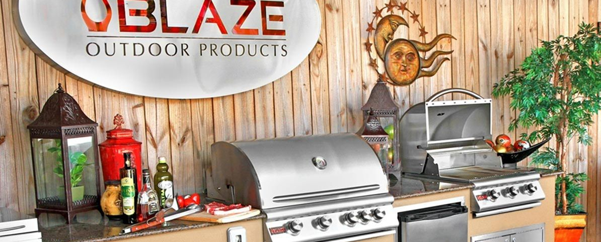 Outdoor kitchen display with Blaze grill, grill accessories, and rustic wooden backdrop