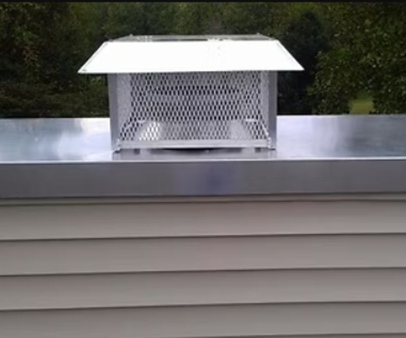 White rooftop vent chimney on a gray roof with a metal chimney cap and wire mesh sides