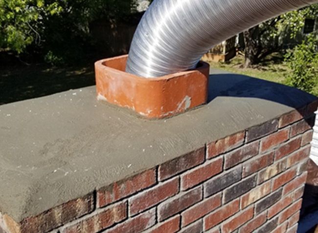 Silver vent pipe through orange roof flashing on a brick chimney for chimney relining