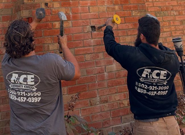 Two certified chimney technicians repairing brick masonry with hammers 