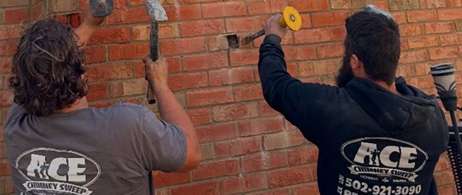 Two workers painting a brick wall with rollers, wearing gray shirts with company logos