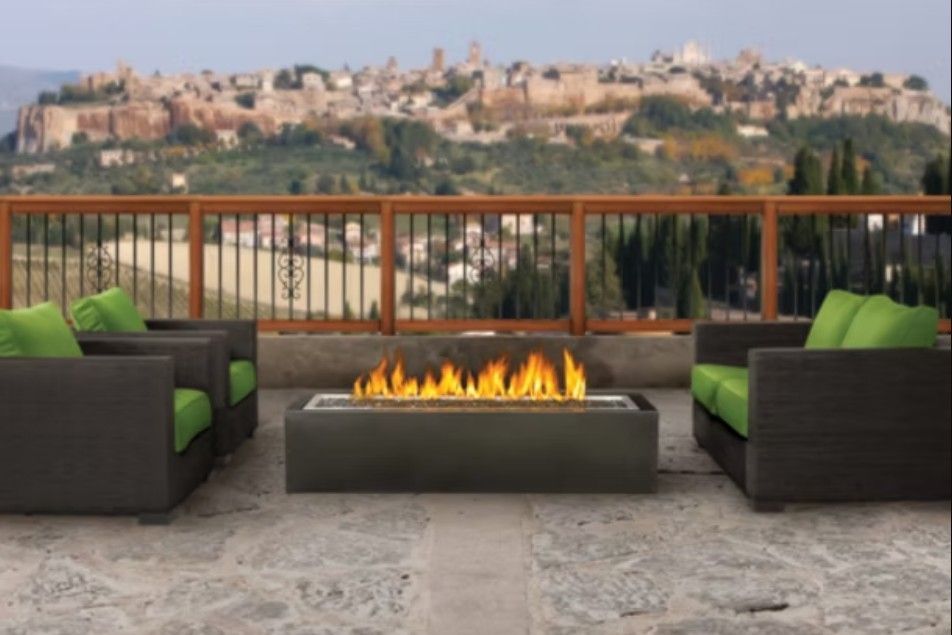 Modern rooftop patio with black wicker chairs, green cushions, and a fire pit overlooking a city skyline