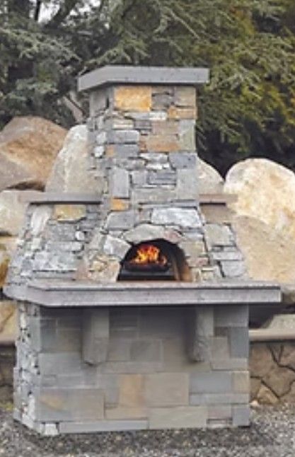 Custom stone outdoor fireplace with a small fire burning inside, set against large rocks and trees
