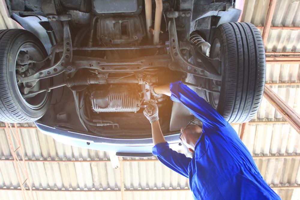 A Man Is Working Under A Car In A Garage — Buddha's Mechanical In Beaconsfield, QLD
