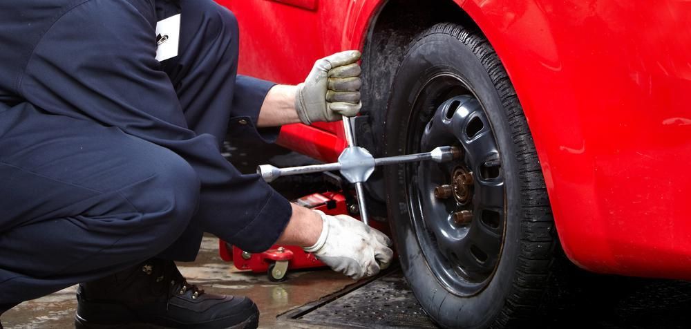 A Man Is Changing A Tire On A Red Car With A Wrench — Buddha's Mechanical In Beaconsfield, QLD