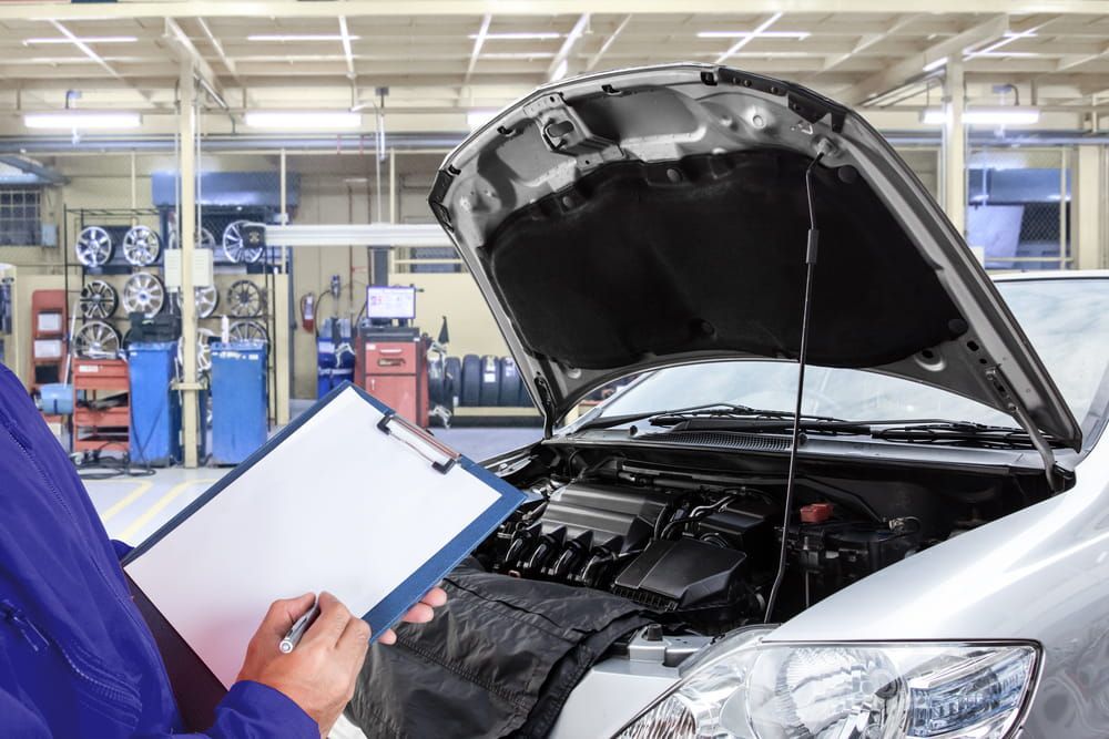 A Mechanic Is Looking At A Clipboard In Front Of A Car In A Garage — Buddha's Mechanical In Beaconsfield, QLD