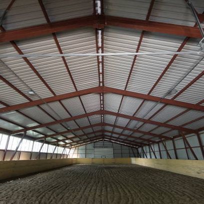 A large indoor arena with a wooden floor and a metal roof.