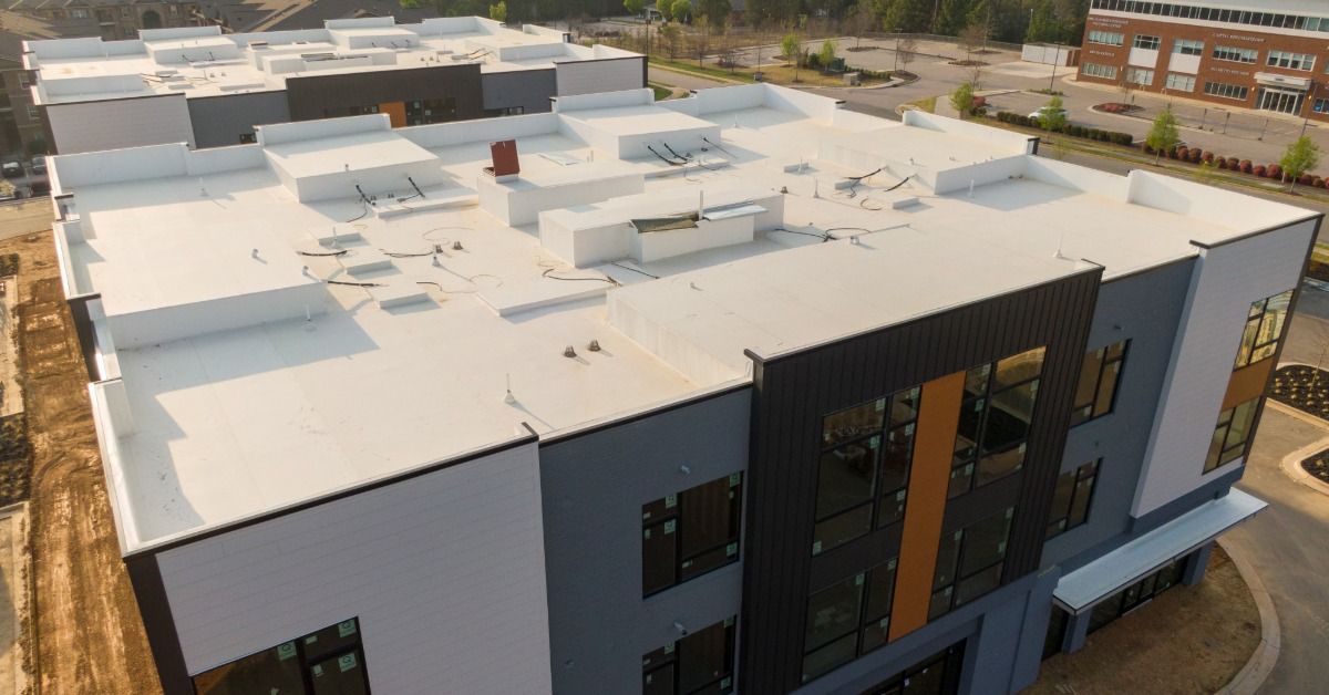 Aerial view of a modern commercial building with a large white flat roof, rooftop equipment, and dar