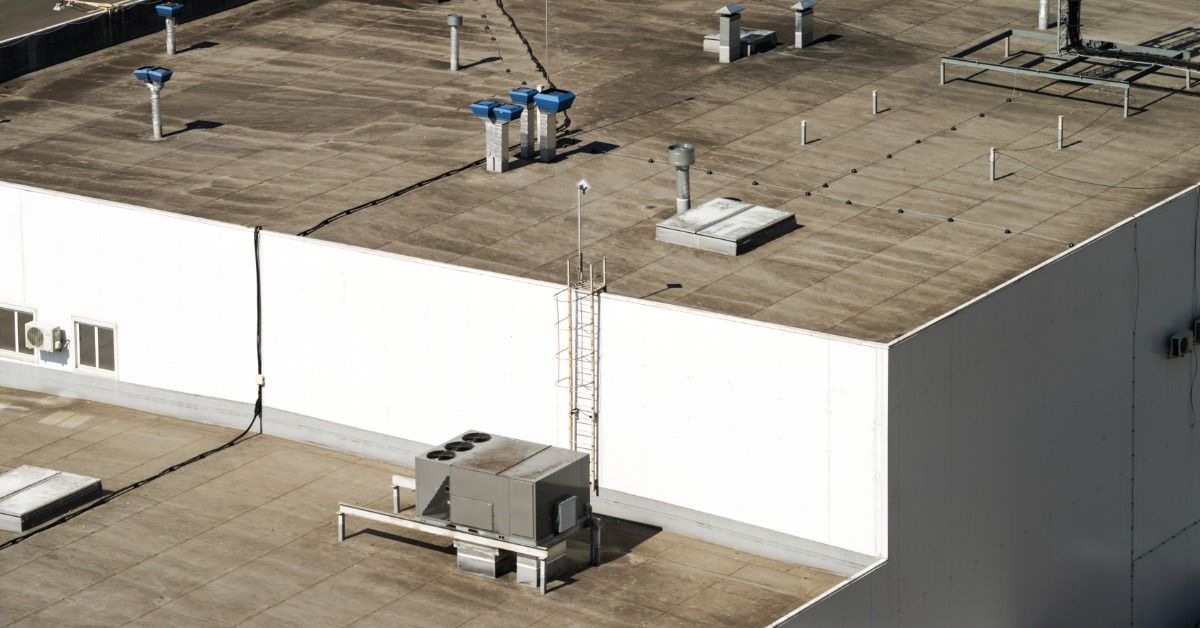 Flat commercial roof with weathered membrane, rooftop vents, HVAC equipment, utility lines, and a roof access ladder.