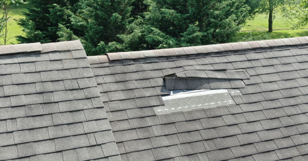 Gray asphalt shingle roof with several missing and damaged shingles exposing underlayment.