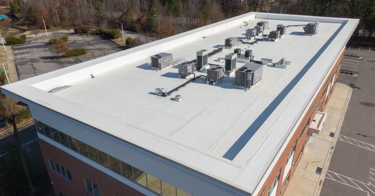 White flat commercial roof with multiple HVAC units atop a large brick office building surrounded by