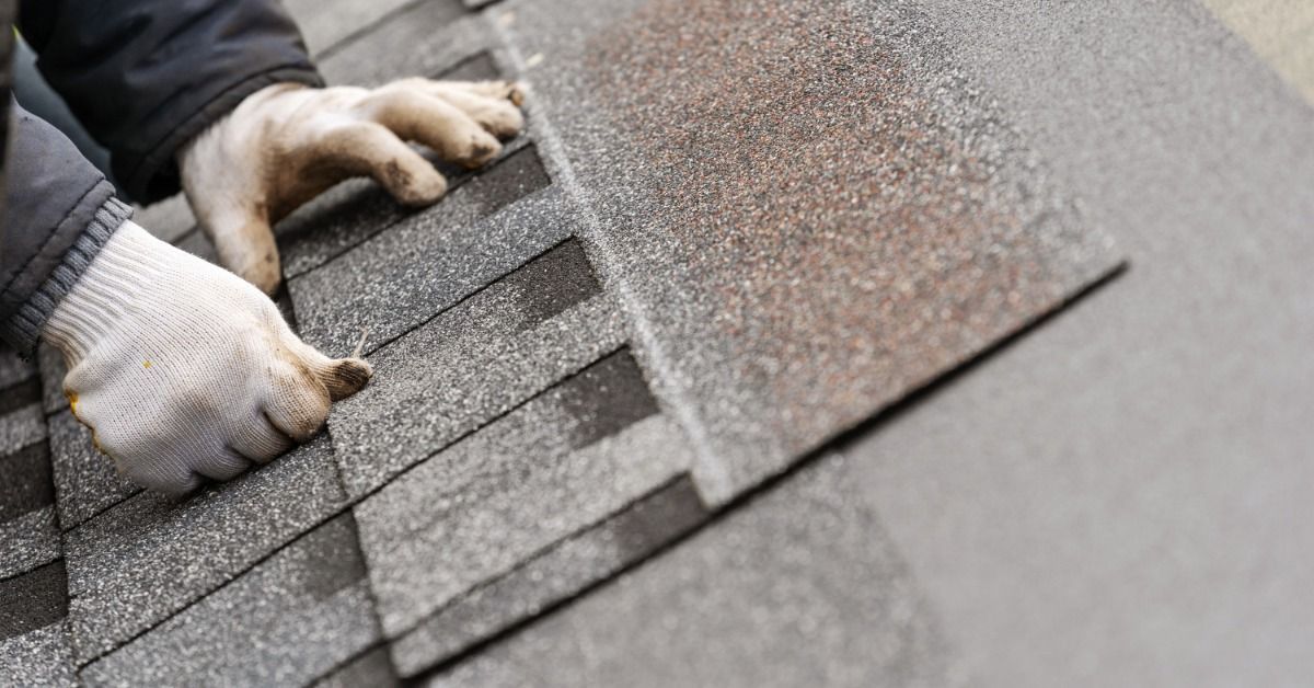 A person in white gloves installing asphalt shingles on a roof, aligning overlapping layers for proper coverage and sealing.
