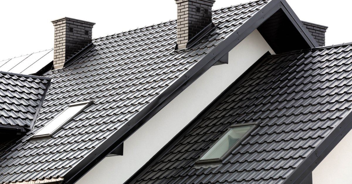 Dark metal roofing covers multiple steep gables with skylights and brick chimneys on a modern residential home.