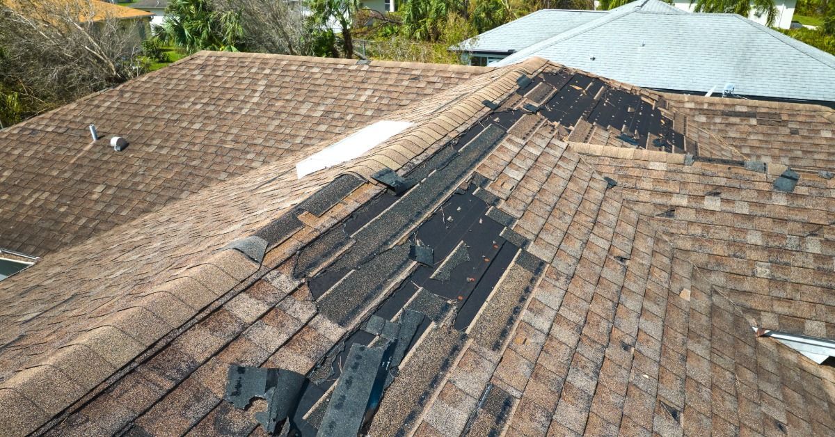 Aerial view of a shingle roof with severe damage, exposing underlayment and missing shingles along the roof ridge.