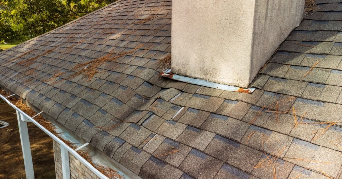 Asphalt shingle roof with lifted shingles and worn chimney flashing, showing common areas where hidden roof leaks begin.