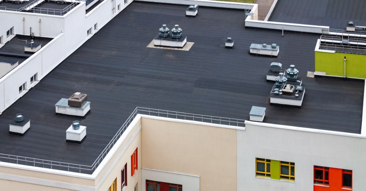 Large commercial building with a black flat roof, rooftop HVAC equipment, vents, and colorful exterior window accents.