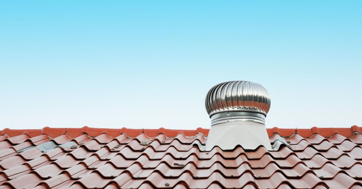 Silver rooftop turbine vent installed on a red tile roof beneath a clear blue sky, providing attic ventilation for the home.