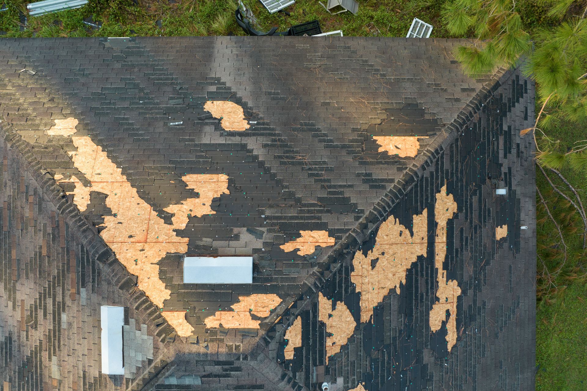 Aerial view of a damaged roof with missing shingles, exposing the underlayment, and debris nearby.