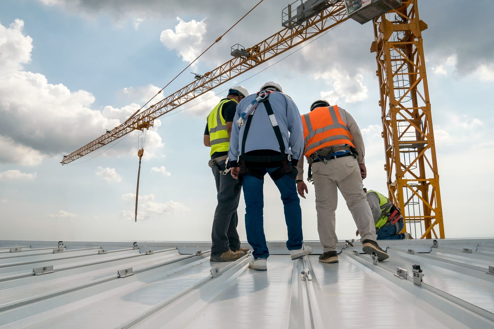 A group of construction workers are working on a roof with a crane in the background.