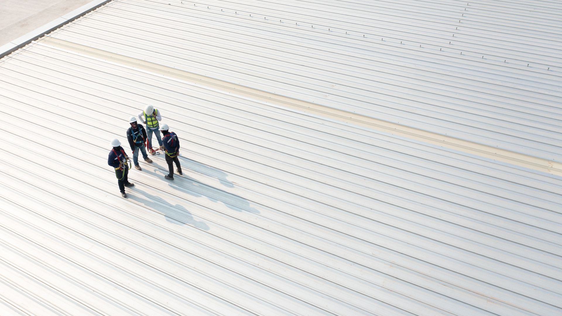 A group of construction workers are standing on top of a white roof.