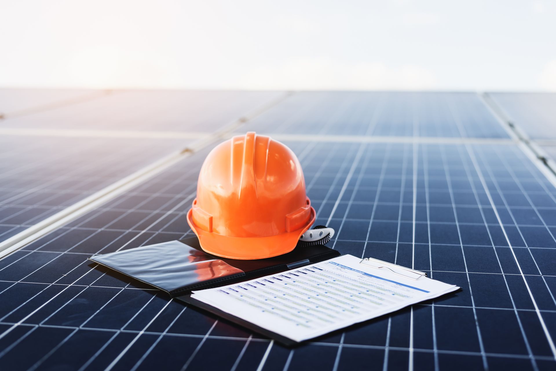 A hard hat and a clipboard are sitting on top of a solar panel.