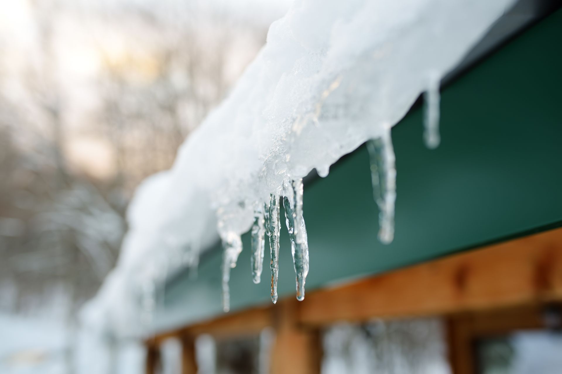 Icicles hanging from a green roof edge, melting in the sunlight.