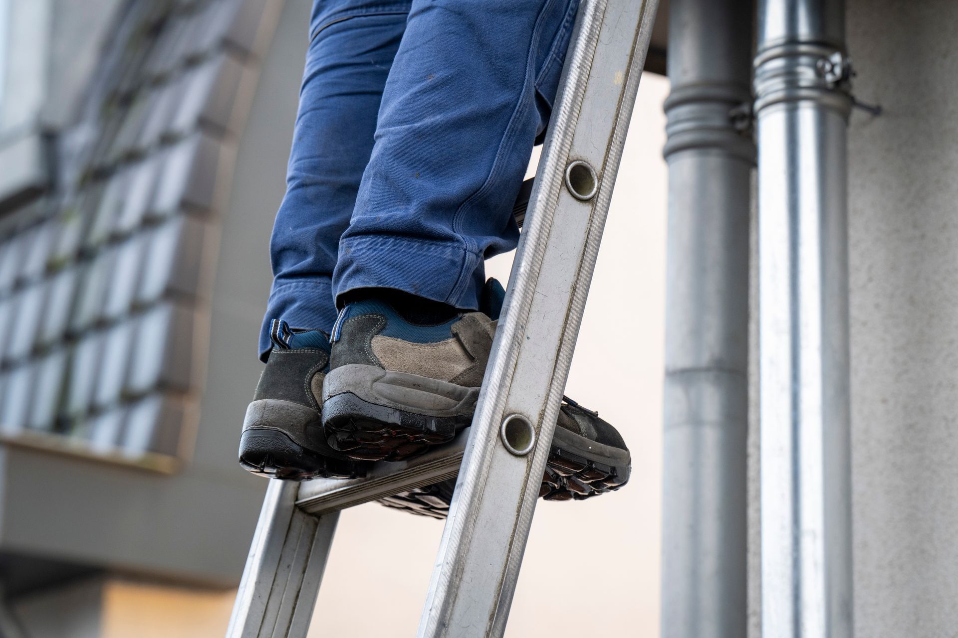 Homeowners feet on a ladder beside metal pipes, wearing jeans and black work boots