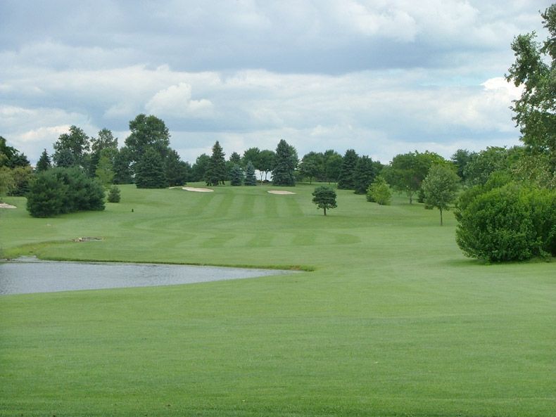 Golf course fairway with a water hazard, trees, and cloudy sky