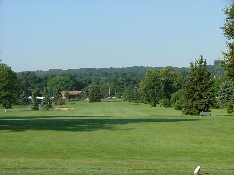 Golf course fairway with trees and distant clubhouse under a clear blue sky