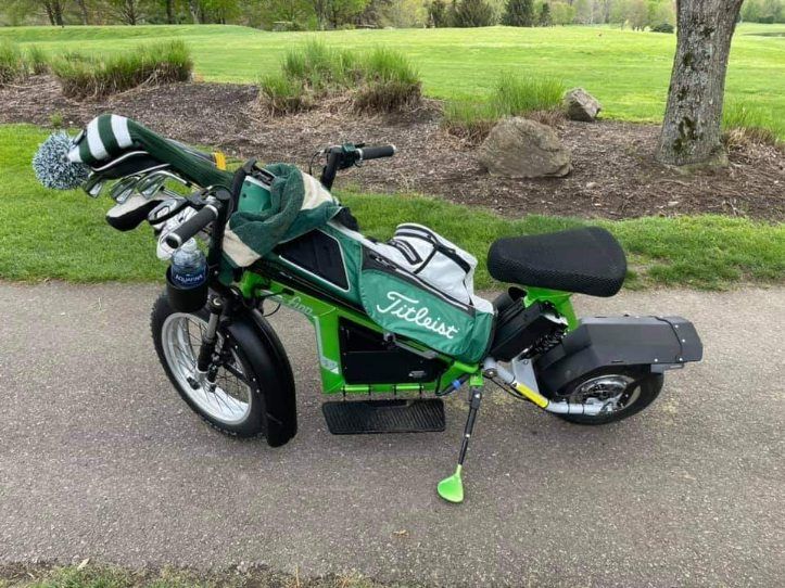 Green golf bag-equipped motorized bike on a paved path beside grass and trees