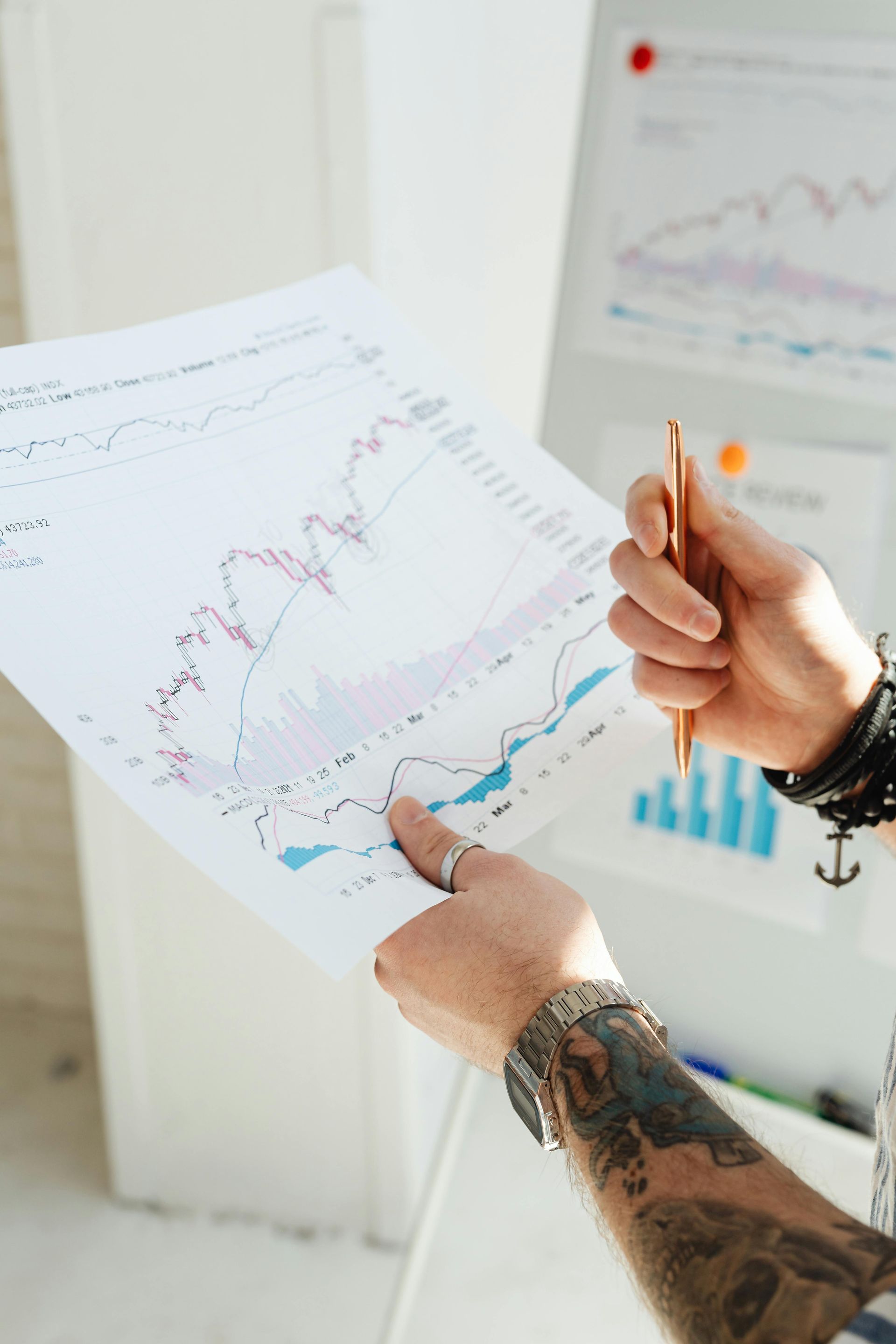 Person holding chart, pointing with pen; whiteboard with graph in background.