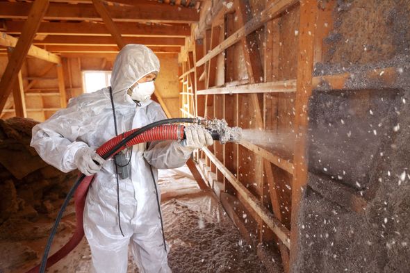 Worker in protective suit spraying insulation inside a wooden attic frame Worker in protective suit spraying insulation inside a wooden attic frame
