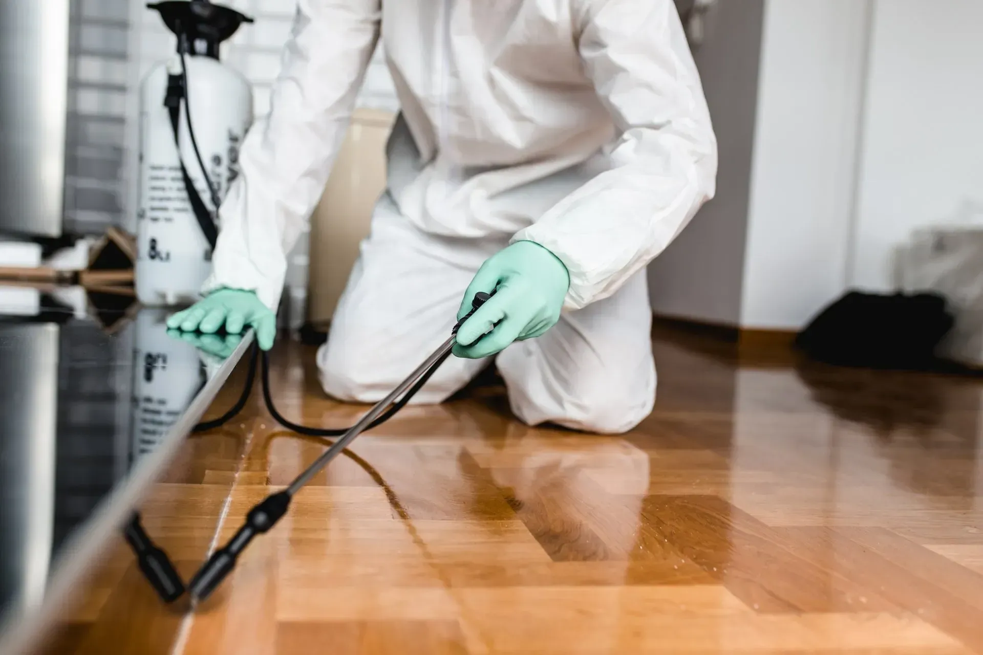 Technician in white coveralls cleaning a hardwood floor with a machine scrubber