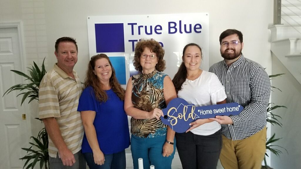 A group of people are posing for a picture in front of a true blue sign.