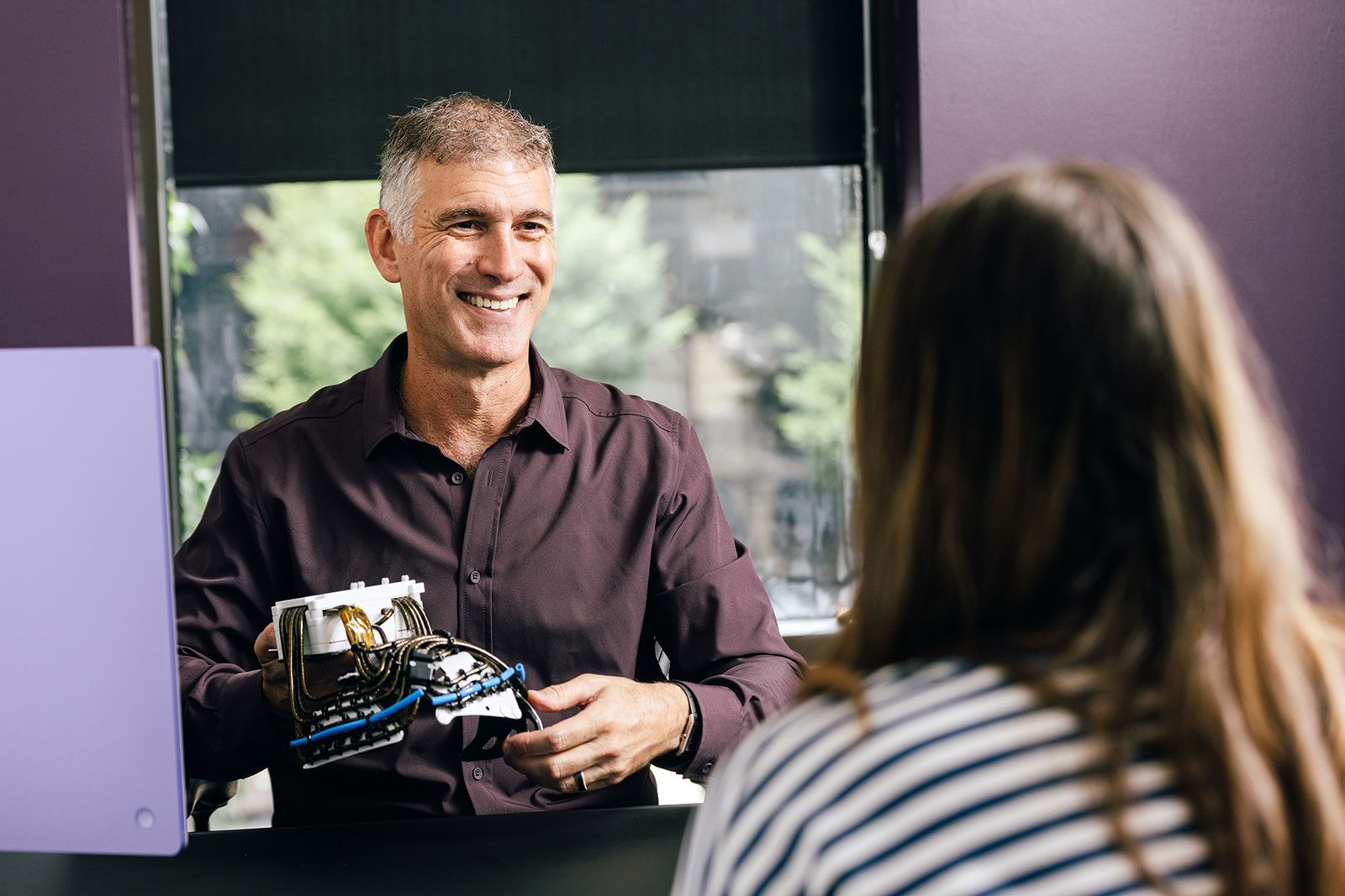 Dr. Roth smiling explaining TMS to young woman. Holding inside of BrainsWay H1 helmet
