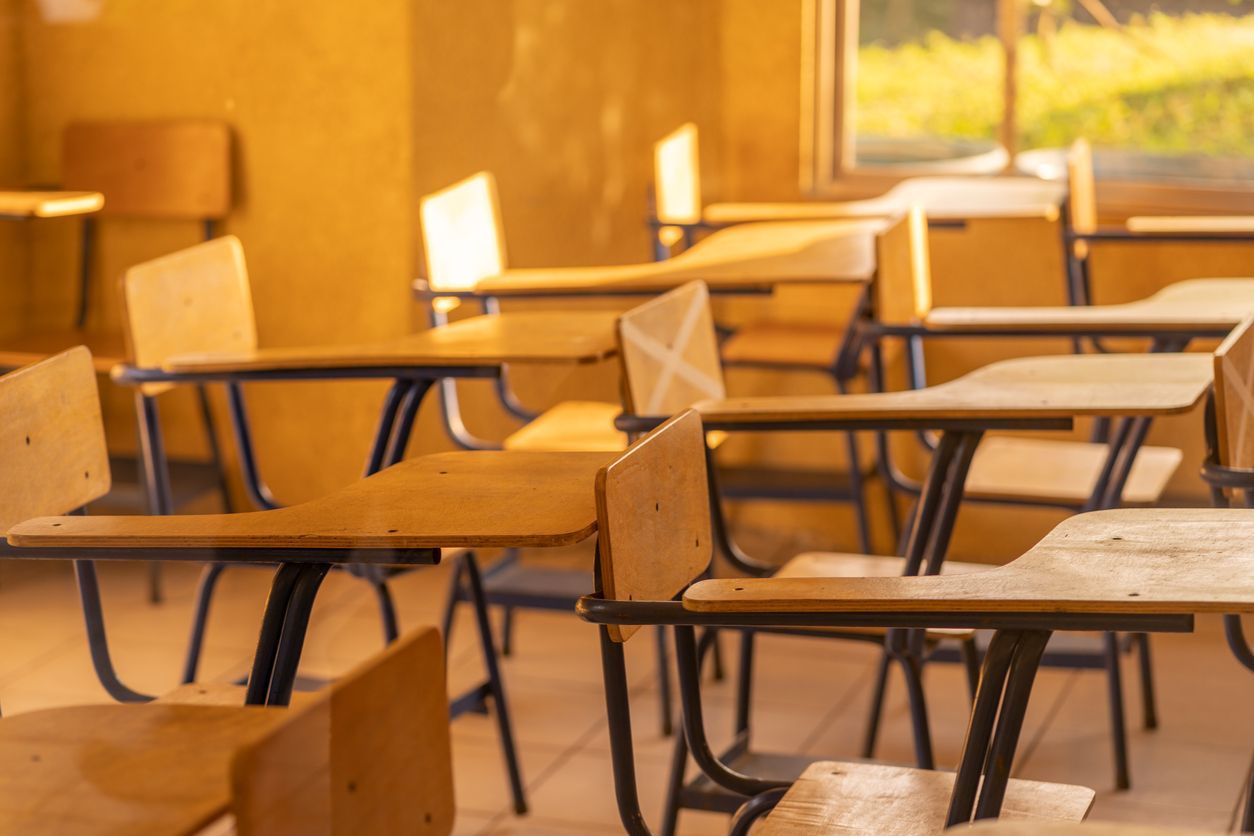Una fila de escritorios y sillas de madera en un aula vacía.