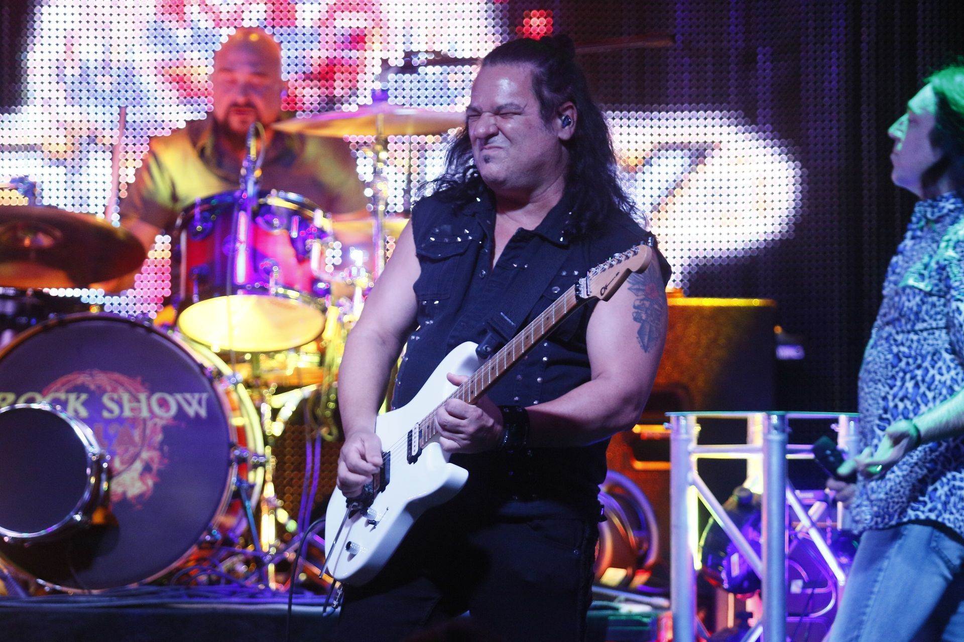 A man is playing a guitar in front of a drum set that says rock show