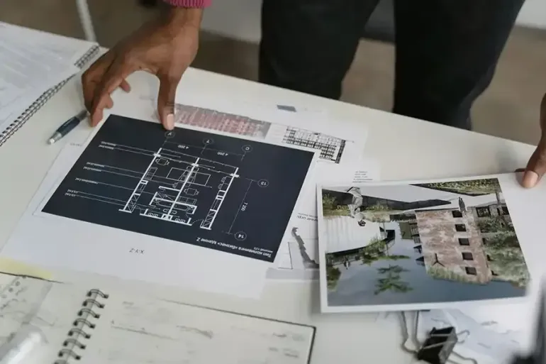 Hands reviewing architectural plans and a building render on a table