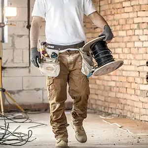 Worker smoothing wet concrete with a trowel at a construction site, with blurred workers in the background