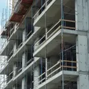 Worker smoothing wet concrete with a trowel at a construction site, with blurred workers in the background