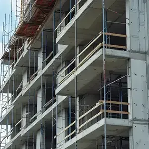 Worker smoothing wet concrete with a trowel at a construction site, with blurred workers in the background