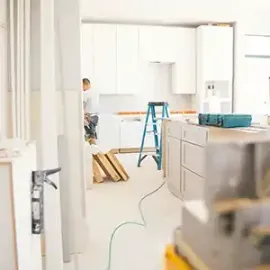 Bright kitchen under renovation with ladder, cabinets, and a person working near the back wall