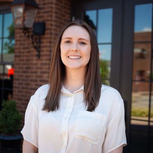 A woman in a white shirt is smiling in front of a brick building