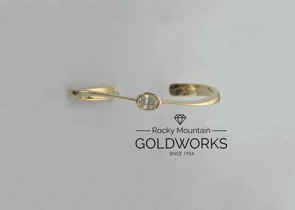 Gold ring with a round center stone above the Rocky Mountain Goldworks logo on a white background