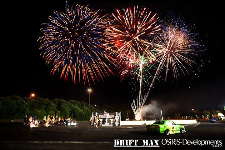A green car is driving in front of a fireworks display. D1NZ