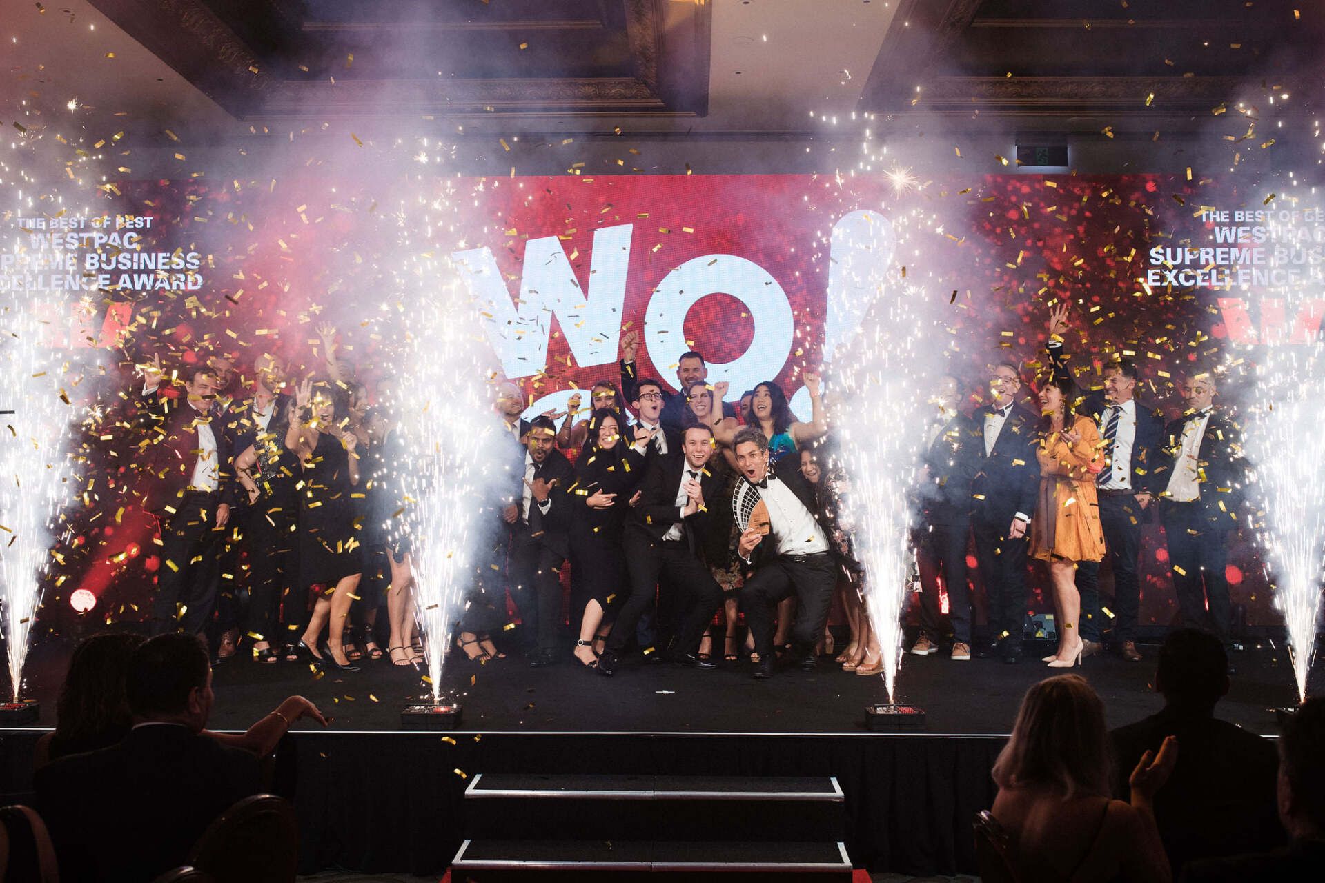A group of people are standing on a stage with fireworks in the background.
