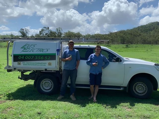 Two Men Are Standing Next To A White Truck In A Field — Levi's Electrics in Nerimbera, QLD